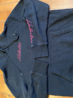 Hollister hoodie - En svart hoodie från Hollister med röda detaljer. Varm och bra nu till kylan.