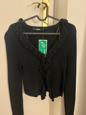 Svart kofta med volang från BikBok - Säljer en snygg svart tröja från bikbok. Aldrig använd. Nypris 400kr. Man kan ha den som både tröja och kofta. 💞💞