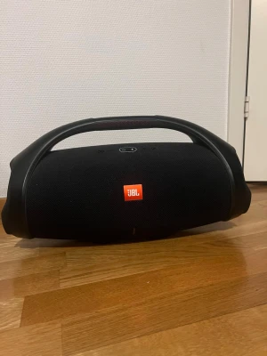 JBL Boombox 2 - Kraftfull JBL Boombox bärbar Bluetooth-högtalare med ikonisk design och robust handtag. Spelar högt och klart, perfekt för både inomhus och utomhus. Skicket är mycket bra och utan synliga skador eller slitage. Endast använt den några få gånger. Lång batteritid på 24 timmar och djup bas för fest och musikupplevelser. Nypris 6000kr. Laddare ingår också.