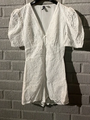 Vit broderad byxdress från H&M Divided - Säljer en söt vit byxdress från H&M Divided i storlek 34. Den har korta puffärmar, v-ringning och är täckt med broderade blommor. Knäppning framtill med tygklädda knappar! Banden är något uttöjda men går enkels att byta ut om man skulle vilja det! Perfekt för student eller skolavslutning!