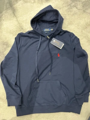 Polo Ralph lauren Hoddie-mörkblå  - Helt ny Polo Ralph lauren Hoddie som aldrig använts, Hoddie är i helt nytt skick utan nån skada eller liknande. Priset kan självklart diskuteras, bara att skicka ett meddelande eller prisförslag. Hodien är liten i storlek så rekommenderas till den som bär storlek M (medium)
