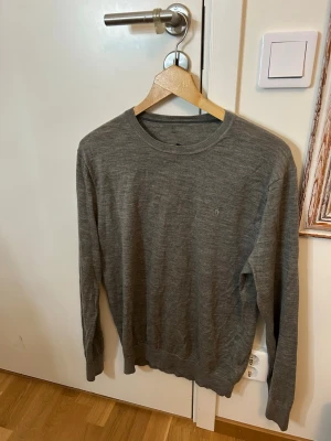 Grå merinoulltröja från Polo Ralph Lauren - Säljer en stilren grå tröja från Polo Ralph Lauren i 100% merinoull. Klassisk rund halsringning, diskret broderad logga på bröstet och långärmad modell. Perfekt till lager på lager under höst och vinter.