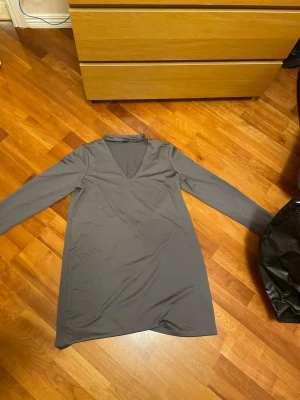 Grå långärmad klänning Gina Tricot - Säljer en enkel och stilren grå klänning från Gina Tricot i storlek L. Klänningen har lång ärm, v-ringning och är gjord i ett mjukt, stretchigt material som känns skönt mot huden. Perfekt att styla med sneakers eller boots. Knappt använd