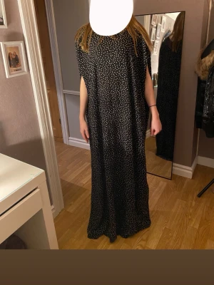 Bati/ klänning  - Säljer en svart lång bati med vitt prickigt mönster. Batin har en loose passform och är ärmlös med rund halsringning. Tyget känns lätt och är jätte skön och ha på sommaren eller bara sova i, perfekt för dig som gillar en avslappnad men ändå snygg stil. Batin är i storlek S men passar egentligen i alla storlekar. 