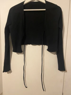 Svart ribbad croppad kofta med knyt - Säljer en svart strechigt, croppad kofta med långa ärmar. 