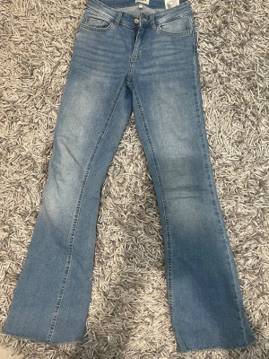 Bootcut jeans från ONLY ljusblå - Säljer ett par ljusblå bootcut jeans från ONLY med klassisk femficksdesign och rå kant längst ner. Jeansen har låg midja och är tillverkade i mjukt denim-material med lätt tvättad look. Storlek xs/30 passar någon under 160 cm lång