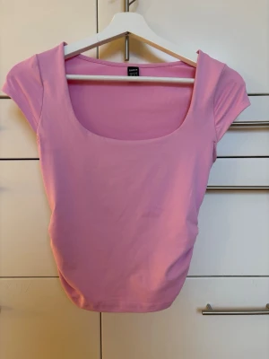 Rosa topp med fyrkantig urringning SHEIN - Säljer en rosa topp från SHEIN i storlek XS. Toppen har en snygg fyrkantig urringning och korta ärmar. Materialet är mjukt och stretchigt i polyesterblandning.