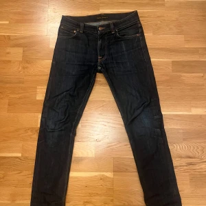 Nudie jeans i modell Lean Dean  - Snygga mörkblå jeans från Nudie Jeans med klassisk orange söm och detaljer på bakfickorna. Modellen har en slim passform och är tillverkad av 100% ekologisk bomull. Perfekt för dig som gillar stilrena och tidlösa jeans med schyssta detaljer.