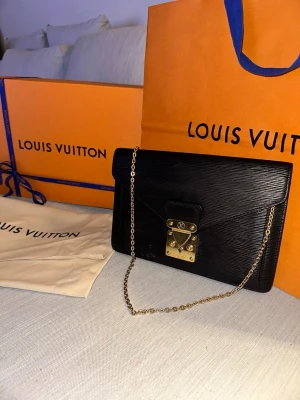 Louis Vuitton Sellier Dragonne  kuvertväska i skinn – Svart Epi Läder (Vintage) - Säljer en exklusiv och elegant Louis Vuitton Sellier Dragonne i klassiskt svart Epi-läder. Detta är en tidlös vintagemodell som kombinerar lyx, kvalitet och funktion – ett perfekt statement-piece för både vardag och fest. - Kan hämtas från Köpenhamn / Malmö.   ✨ Detaljer: * Märke: Louis Vuitton * Modell: Sellier Dragonne * Färg: Svart * Material: Epi Läder * Serienummer: TH0977 * Tillverkad i Frankrike * Bredd: ~ 16 cm * Längd: ~ 26,5 cm   ✨ Skick: Väskan är i mycket bra vintage skick: 