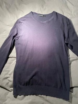 Mörkblå stickad tröja J.Lindeberg - Snygg mörkblå stickad tröja från J.Lindeberg med diskret logga på bröstet. Tröjan har rund hals, långa ärmar och ribbade muddar vid ärmslut och nederkant. Perfekt för dig som gillar stilrena och klassiska plagg. Bra skick!