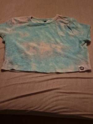 Blå croppad frottétopp H&M Lazy Wave - Säljer en croppad topp från H&M x Lazy Wave Surf Club i mjuk frotté. Toppen har korta ärmar och ett blått och vitt batikmönster som ger en chill vibe. Perfekt till sommaren och strandhäng. Märke på nederkanten. Den är gjort av handduks material, perfekt för efter en dusch, bad eller en simtur med kompisarna under sommaren. Nästan helt oanvänd. Priset kan diskuteras🫶