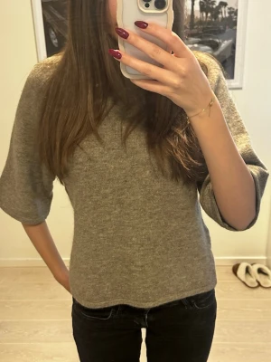 Beige stickad tröja med trekvartsärm - Mysig beige stickad tröja med trekvartsärm och rund hals. Tröjan har en avslappnad passform och ribbad kant vid halsen. Perfekt för lager på lager under kyliga dagar.