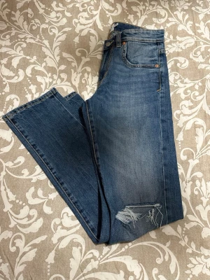 Blå slim jeans från Lager 157, storlek 30/32 - Snygga blå jeans från Lager 157 med slim passform och klassisk femficksdesign. Jeansen har slitna detaljer vid knäna och raka ben. Materialet är jeans med tydliga kontrastsömmar. Perfekt för dig som gillar en avslappnad men trendig look.