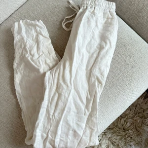 Vita linnebyxor från Design by Si - Säljer ett par vita linnebyxor från Design by Si i storlek S. Byxorna har resår och snörning i midjan för skön passform. Aldrig använda