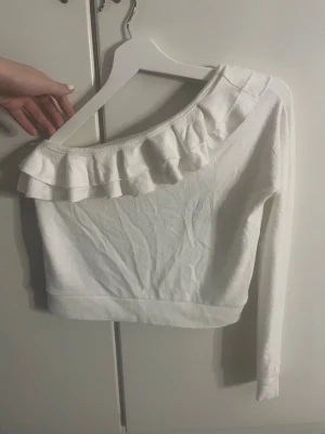 Volang tröja - Säljer en vit topp från Chiquelle i storlek S. Toppen har en offshoulder-design med bred volang längs halsringningen och långa ärmar. 