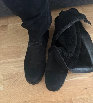 Mockastövlar  - Svarta mockastövlar med dragkedja på på sidan med mjukt foder på insidan.Höjd är ca 45–47 cm och klackhöjden ligger runt 6 cm. Perfekt för kalla dagar