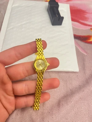 Guldfärgad elegant damklocka Charybdis - Snygg guldfärgad damklocka från Charybdis med klassisk rund urtavla och länkarmband i metall. Urtavlan är ljus med tydliga siffror och quartz-verk. Perfekt accessoar för dig som gillar stilrena detaljer och guldtoner.