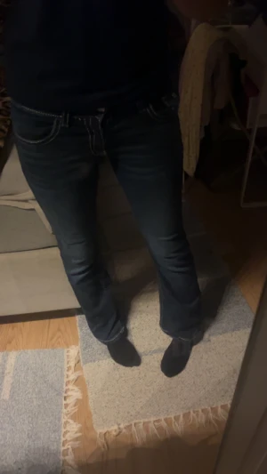 Mörkblå bootcut jeans med kontrastsömmar - Snygga mörkblå jeans med bootcut passform och tydliga vita kontrastsömmar. Byxorna har låg midja, klassiska fem fickor och dekorativa knappar på bakfickorna. Jeansen är tillverkade i jeansmaterial och har en stilren look som passar perfekt till sneakers eller boots.