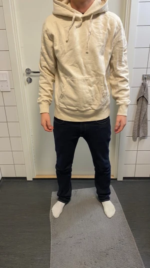 Beige hoodie med magficka - Säljer en stilren beige hoodie i mjukt material med stor huva och dragsnören. Hoodien har en klassisk magficka framtill och ribbade muddar vid ärmslut och nederkant. Perfekt för chill dagar och enkel att matcha med jeans eller joggers.