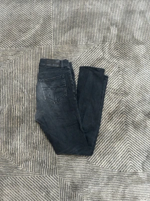 Svarta jeans från Tiger of Sweden - Säljer ett par svarta skinny jeans från Tiger of Sweden med klassisk femficksdesign och smal passform. Jeansen har hög midja, svarta sömmar och en diskret logotyp vid fickan. Materialet är stretchigt denim för extra komfort.