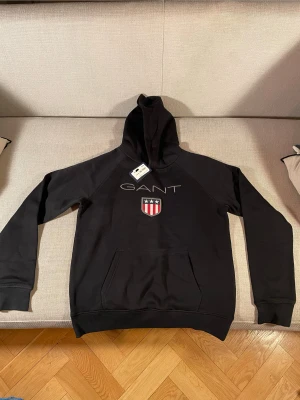 Helt ny GANT Hoodie - En helt ny Gant hoodie som aldrig vart använd. Hoodien har prislappen kvar.  Är för 13-14 åringar med längden 158-164cm. Priset ligger på 700kr, skriv vid behov av flera bilder eller flera funderingar!