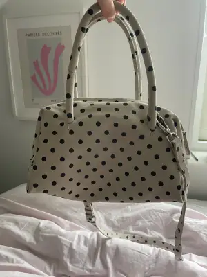 Snygg handväska från Zara i vit mocka med svarta prickar. Väskan har två handtag, avtagbar axelrem och dragkedja upptill. Insidan är svart med en innerficka med dragkedja. Perfekt storlek för det viktigaste och sticker ut med sitt coola prickiga mönster. Aldrig använd och köpt för 999kr.