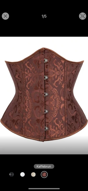 Kaffeebrun brokad korsett med snörning - Säljer en snygg kaffeebrun korsett med brokadmönster och metallknappar framtill. Baksidan har bred snörning med satinband för perfekt passform. Korsetten har en markerad midja och klassisk form som ger en cool siluett.