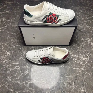 Gucci vita sneakers med orm brodyr - Säljer ett par vita sneakers från Gucci i skinn med ikonisk röd och grön orm brodyr på sidan. Skorna är lite mer skadade i verklighet 