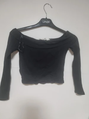 Svart offshoulder croppad topp H&M - Säljer en svart croppad topp från H&M med offshoulder-design och långa ärmar. Toppen är ribbad och har en snygg, figurnära passform som framhäver axlarna. Perfekt för dig som gillar stilrena och trendiga plagg.