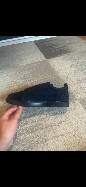 Louboutins - Snygga mörkblå sneakers från Christian Louboutin med klassisk röd sula och broderad logga på hälen. Skorna har rund tå, snörning och är tillverkade i mocka med skinnfoder. Perfekt för dig som vill sticka ut med exklusiva detaljer och stilren design.