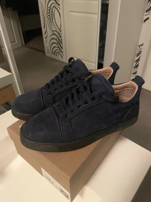 Louboutin  - Snygga mörkblå sneakers från Christian Louboutin i mjuk mocka med klassiska röda sulor och rund tå. Skorna har svarta snören och en stilren design med beige innersida. Perfekta för dig som vill ha en lyxig och unik look.