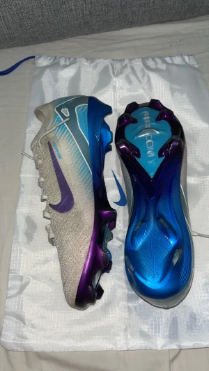 Nike Mercurial fotbollsskor blå/lila - Säljer ett par Nike Mercurial fotbollsskor i en futuristisk design med silverfärgad ovandel, lila Swoosh och blå detaljer. Skorna har snörning och en cool, skimrande blå och lila sula. Perfekta för dig som vill sticka ut på planen! Obs dom är kopior