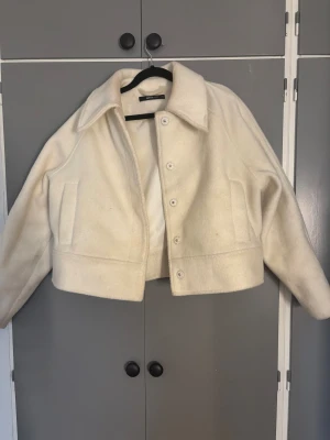 Vit teddyjacka från Gina Tricot - Säljer en vit teddyjacka från Gina Tricot i storlek S. Jackan är croppad med klassisk krage, knappar framtill och två sidofickor. Mjuk och fluffig känsla, perfekt för att addera lite cozy vibes till din outfit.