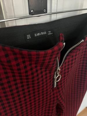 Röd-rutiga leggings från Zara - Snygga röd- och svart-rutiga leggings från Zara med hög midja och silverfärgad dragkedja baktill. Stretchigt mjukt material, sitter tight och är supersköna att bära. Modern punkig look. Funkar perfekt till tisha eller skjorta, och som bas till svart kavaj, eller till lång stickad tröja för att ge mer avslappnad mysfaktor. Modellen på bilderna  är strl 36/S vilket bättre motsvarar passformen än angiven strl M. 