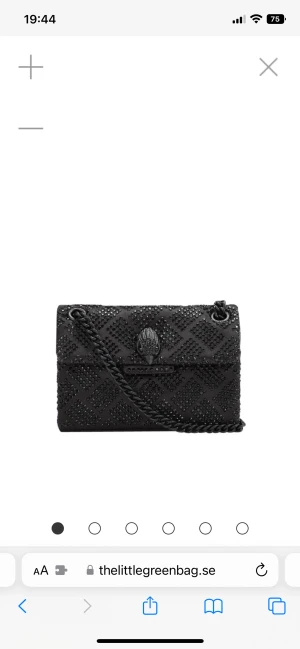 Svart axelväska från Kurt Geiger - Snygg svart axelväska från Kurt Geiger med glittriga svarta stenar i rutmönster och en cool kedja som axelrem. Väskan har ett unikt örndekor på locket och är tillverkad i mjukt syntetmaterial. Perfekt för att lyfta din outfit med lite extra edge.