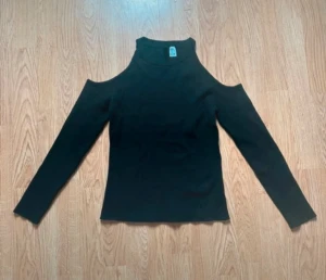 Svart långärmad topp med offshoulder - Säljer en svart långärmad topp med ribbad struktur och snygg offshoulder-design som visar axlarna. Modellen är figurnära med hög hals och ger en cool och modern vibe. Perfekt att styla med jeans eller kjol för en trendig look