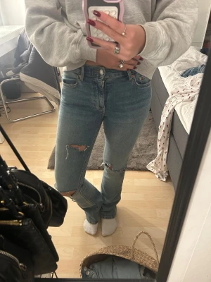 Blå jeans från Gina tricot  - Snygga blå jeans från Gina tricot i storlek 34 med egnagjorda hål på. Modellen har klassisk femficksdesign, normal passform och raka ben. Perfekt för dig som gillar en avslappnad och trendig look.