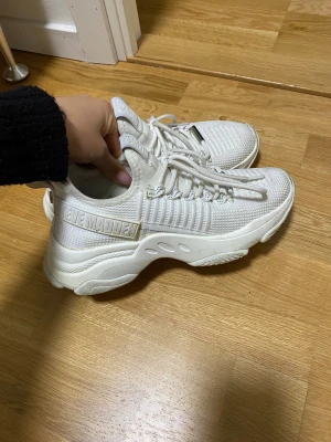 Chunky vita sneakers Steve Madden - Säljer ett par chunky vita sneakers från Steve Madden med stickad ovandel och tjock sula. Skorna har snörning och coola detaljer med logga på hälen och plösen. Perfekta för dig som gillar sportig och trendig stil.