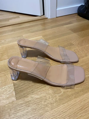 Beiga sandaler med transparent klack - Säljer ett par trendiga sandaler i beige med transparenta remmar och klack. Skorna har fyrkantig tå och en låg, genomskinlig klack som ger en modern vibe. Perfekta för dig som gillar stilrena och minimalistiska detaljer.