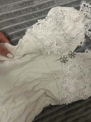 Vit spetsklänning med pärldetaljer - En jättefin vit kort klänning som är tajt och är från Rare London som är ett jättebra märke till klänningar och är desutom väldigt dyrt. Går till student ,fest bröllop 🤍