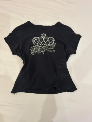 Svart Respect M.E. t-shirt från Adidas - Cool croppad t-shirt från Adidas Respect M.E. med ett stort tryck av en krona och texten 'Respect m.e.' på bröstet. Modellen är kortärmad och har en klassisk rund hals. Materialet är mjuk bomull som känns skönt mot huden.