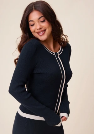 Mörkblå ribbad kofta med vita detaljer - Snygg mörkblå ribbad kofta med vita kontrastdetaljer i storlek 36/38 längs knäppningen, halsringningen och nederkanten. Koftan har rund hals, långa ärmar och knappar framtill. Perfekt för dig som gillar en stilren och klassisk look. Säljer den då det inte är min stil och har gått för långt tid för att kunna skicka tillbaka.