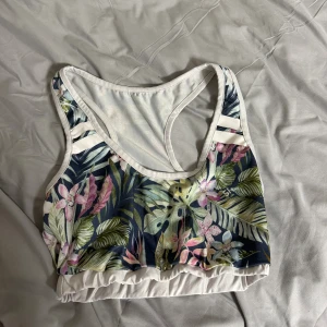 Stronger topp - Säljer en fräsch linnetopp med tropiskt blommigt mönster i grönt, rosa, vitt och blått. Toppen har breda axelband och vit kant runtom, samt elastisk nederkant för skön passform. Perfekt för dig som gillar färg och mönster!