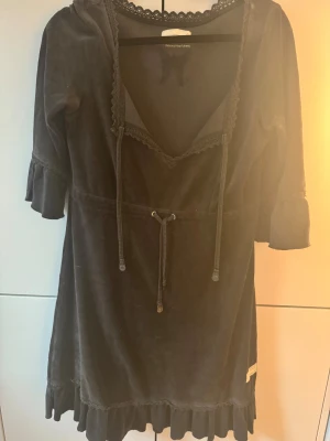 Grå plysch/sammetklänning Odd Molly - Supersöt grå kortklänning från Odd Molly i mjuk plysch/sammet med v-ringad hals, spetsdetaljer och snörning i midjan. Klänningen har trekvartsärmar med volang och volangkant nedtill. Perfekt för dig som gillar boho-vibe och vill ha något unikt i garderoben. Fin till julen. 