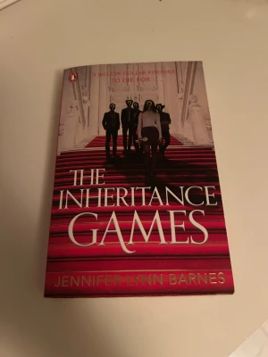 The Inheritance Games - En spännande bok med mystik och gåtor, perfekt för dig som gillar intriger och oväntade vändningar. Omslaget visar en grupp personer på röda trappor, vilket ger en känsla av lyx och hemligheter. Passar dig som vill ha en fängslande och modern berättelse.