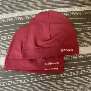 Vinröd mössa från Kalenji - Snygg vinröd mössa från Kalenji, perfekt för dig som gillar att träna utomhus. Mjuk och stretchig syntetmaterial som sitter skönt på huvudet. Diskret logga framtill. Enkel design som funkar till sportiga outfits.