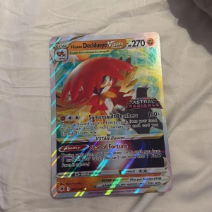 Hisuian Decidueye VSTAR stor  - Cool och glittrig Pokémonkort från Astral Radiance-serien! Hisuian Decidueye VSTAR har 270 HP och unika attacker som Somersault Feathers och Star of Fortune. Perfekt för samlare och Pokémon-fans som vill boosta sin kortlek med en kraftfull och snygg VSTAR. Stort kort