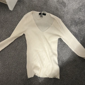 Vit ribbad långärmad topp V-ringad - Säljer en vit ribbad långärmad topp från vero moda med snygg v-ringning och lätt vågig kant nertill. Toppen är figurnära och stretchig, perfekt att styla med jeans eller kjol. Enkel och stilren design som passar till många olika looks. 