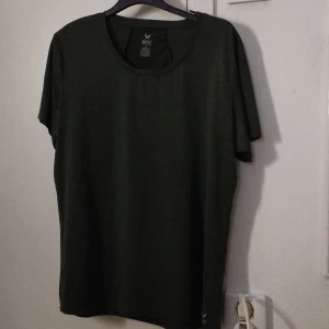 Grön tränings-tshirt från SOC - Mörkgrön t-shirt från SOC i storlek L, perfekt för träning. Tillverkad i ett lätt och syntetiskt material med meshpanel på ryggen för extra ventilation. Klassisk rund hals och korta ärmar. Enkel och sportig design.