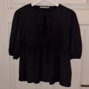 Denna tröjan har jag använd 1 gång men den har inte riktigt varit min stil d skulle va kul om någon annan skulle kunna ha den  - Svart blus från 157 med rund halsringning och knyt framtill. Blusen har puffiga trekvartsärmar och en volang nedtill som ger en flowy siluett. Perfekt för dig som gillar en enkel men snygg look med lite extra detaljer.